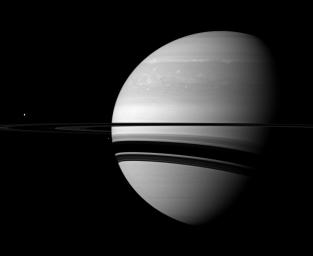 A pair of Saturn's many moons joins the planet in this scene captured by NASA's Cassini spacecraft. Tethys appears as a small white dot above the rings on the far left, Enceladus appears as a smaller bright speck beside the planet.