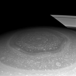 Saturn's north polar hexagon basks in the Sun's light now that spring has come to the northern hemisphere. Many smaller storms dot the north polar region and Saturn's signature rings put in an appearance in the background.