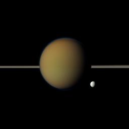 Saturn's moon Tethys, with its stark white icy surface, peeps out from behind the larger, hazy, colorful Titan in this view of the two moons obtained by NASA's Cassini spacecraft. Saturn's rings lie between the two.