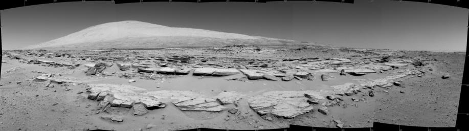 A landscape scene from NASA's Curiosity Mars rover shows rock rows at 'Junda' forming striations in the foreground, with Mount Sharp on the horizon.