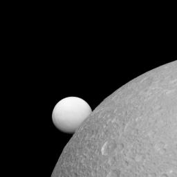 Although Dione (near) and Enceladus (far) are composed of nearly the same materials, Enceladus has a considerably higher reflectivity than Dione. As a result, it appears brighter against the dark night sky as seen by NASA's Cassini spacecraft.