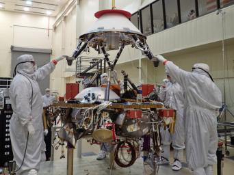 In this photo, spacecraft specialists at Lockheed Martin Space Systems, Denver, are reaching up to guide lowering of the parachute cone for installation onto NASA's InSight spacecraft. The photo was taken on April 29, 2015.