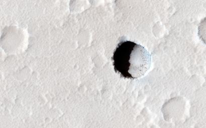This image, taken by NASA's Mars Reconnaissance Orbiter spacecraft, is of an area on the lower southeastern flank of the volcano Elysium Mons. A small, dark pristine-appearing pit is clearly visible among the numerous small impact craters.