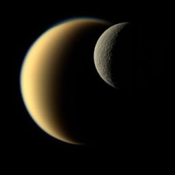 In this view, Saturn's icy moon Rhea passes in front of Titan as seen by NASA's Cassini spacecraft. While Rhea is a heavily-cratered, airless world, Titan's nitrogen-rich atmosphere is even thicker than Earth's.