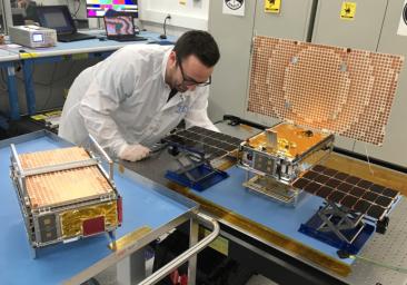 Engineer Joel Steinkraus stands with both of the Mars Cube One (MarCO) spacecraft at NASA's Jet Propulsion Laboratory.