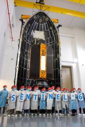 Technicians and engineers working on the Sentinel-6 Michael Freilich satellite pose in front of the spacecraft in its protective nosecone, or payload fairing, at Vandenberg Air Force Base in California.