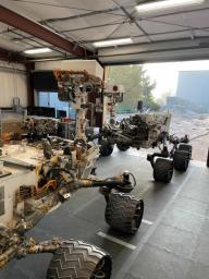 Engineering models of the Curiosity Mars rover (foreground) and the Perseverance Mars rover share space in the garage at JPL's Mars Yard.