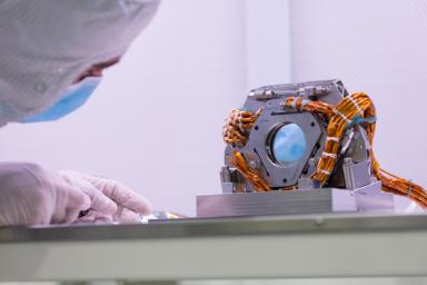 An engineer examines the fast steering mirror, part of the Coronagraph Instrument's optical bench. The mirror makes small movements that correct for slight wobbling of the Roman spacecraft.