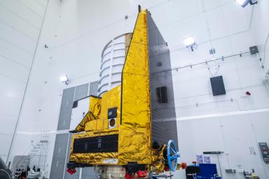 The ESA Euclid telescope is shown in a clean room before launch. Black solar panels line the right side of the spacecraft. The telescope will view the cosmos through the top of the white cylinder that sits above the spacecraft's instruments.
