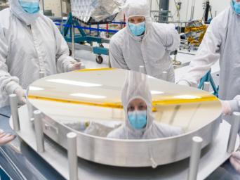 A mirror that was later installed inside the telescope for NASA's NEO Surveyor shows a reflection of principal optical engineer Brian Monacelli during an inspection of the mirror's surface.