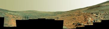 This panorama shows two rock-strewn slopes on the left and right sides of a broad, U-shaped dip in the middle. The sandy surface in front of the rover is reddish brown; individual rocks and more distant features are blue-gray.