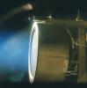 This image of a xenon ion engine prototype, photographed through a port of the vacuum chamber where it was being tested at NASA's Jet Propulsion Laboratory, shows the faint blue glow of charged atoms being emitted from the engine.
