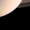 Saturn's atmosphere is prominently shown with the rings emerging from behind the planet at upper right. The two moons on the left of the image, Mimas and Enceladus, were captured by NASA's Cassini spacecraft.