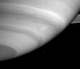 This image captured by NASA's Cassini spacecraft shows a tiny Mimas, dwarfed by a huge white storm and dark waves on the edge of a cloud band in Saturn's atmosphere.