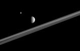 Two of Saturn's battered, icy companions, Tethys and Mimas, hover here, above the ringplane. A wide band of visible rings is in between the two moons in this view from NASA's Cassini spacecraft.