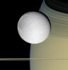 Speeding toward pale, icy Dione, Cassini's view is enriched by the tranquil gold and blue hues of Saturn in the distance. The horizontal stripes near the bottom of the image are Saturn's rings.