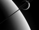 This view was taken from above the ringplane and looks toward the unlit side of the rings. Here, the probe gazes upon Titan in the distance beyond Saturn and its dark and graceful rings as seen by NASA's Cassini spacecraft.
