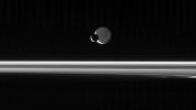 NASA's Cassini spacecraft looks across the unlit ringplane as Mimas glides silently in front of Dione.