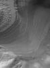 NASA's Mars Global Surveyor shows a mound of layered rock in places over-ridden by dark sand dunes occurring immediately south of the 'mouth' of Gale Crater (also know as 'Happy Face Crater') on Mars. Groups of layers cut across each other in places.