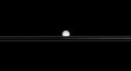 From a low angle above Saturn's rings, NASA's Cassini spacecraft's view of an icy moon is partly obscured. The view looks toward Enceladus across the unilluminated side of the rings from less than a degree above the ringplane.