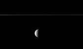 From just below the plane of Saturn's rings, NASA's Cassini spacecraft looks at the rings edge-on and sees the planet's second largest moon beyond. Although Rhea may appear to be in the foreground of this image, it is not.