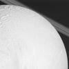 NASA's Cassini spacecraft looks over cratered and tectonically deformed terrain on Saturn's moon Enceladus as the camera also catches a glimpse of the planet's rings in the background.