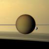 Saturn's fourth-largest moon, Dione, can be seen through the haze of the planet's largest moon, Titan, in this view of the two posing before the planet and its rings from NASA's Cassini spacecraft.
