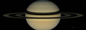 Saturn's rings cast dark bands across cloud tops in the northern hemisphere. Near the pole, an elongated shadow can be seen from Saturn's moon Tethys. Icy moons Dione (front right) and Enceladus (back right) are also seen by NASA's Cassini spacecraft.