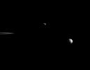 Saturn's moons Janus and Mimas coast in their silent orbits beyond the rings in this view from NASA's Cassini spacecraft. The ansa, or outer edge of the rings, is visible at left.