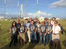 NASA's Optical PAyload for Lasercomm Science (OPALS) operations team at Kennedy Space Center's Space Launch Complex-40 on April 14, 2014, with the SpaceX Falcon 9 rocket carrying OPALS in the background.