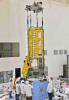A crane is used to align NISAR's radar instrument payload, seen partially wrapped in gold-colored thermal blanketing, with the satellite's spacecraft bus, which is inside blue blanketing, in an ISRO clean room in Bengaluru, India, in June, 2023.